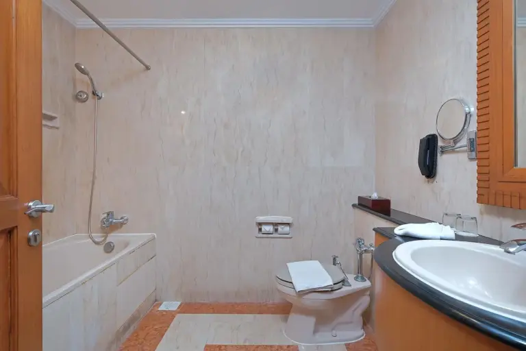 Bathroom at Sunlake Waterfront Resort & Convention Jakarta with bathtub, toilet, sink, and beige marble finishes