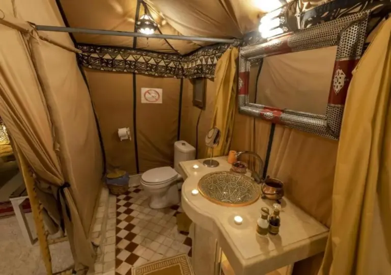 Tent bathroom at Sunset Dunes Camp in Merzouga with toilet, sink, mirror, and enclosed shower area.