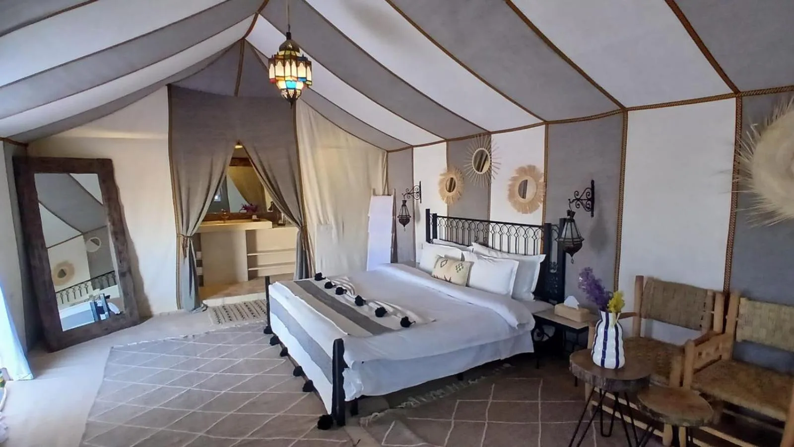 Suite tente Deluxe au Sunshine luxury desert camp à Merzouga avec un plafond de style baldaquin, un coin salon et un grand lit.