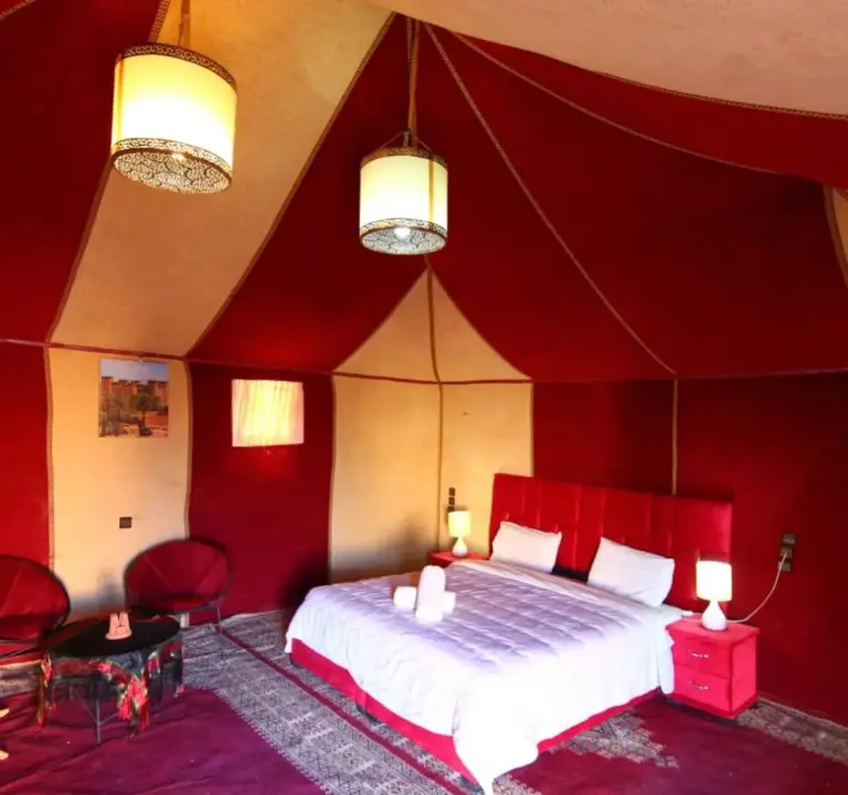 Suite tente de luxe au Sunshine luxury desert camp à Merzouga avec un décor rouge et beige, des lampes suspendues et un lit king size.