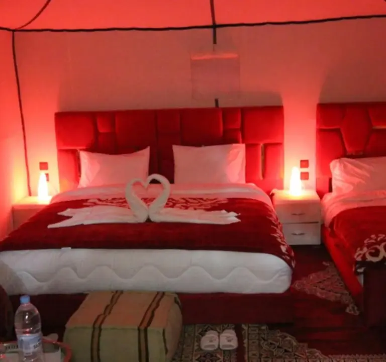 Tente triple au Sunshine luxury desert camp à Merzouga avec éclairage rouge, lits assortis et décoration romantique avec serviettes.