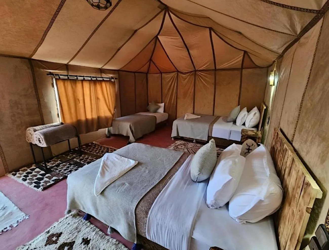 Sunshine luxury tent in Merzouga family tent room with multiple beds, patterned rugs, and natural canvas walls.
