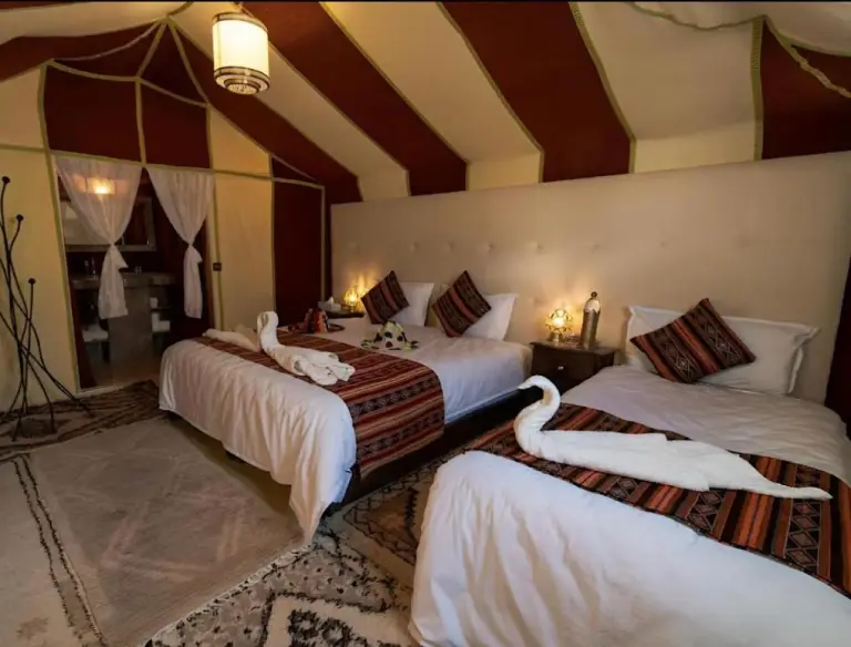 Sunshine luxury tent in Merzouga triple suite with three beds, soft lighting, and a spacious canvas bedroom.