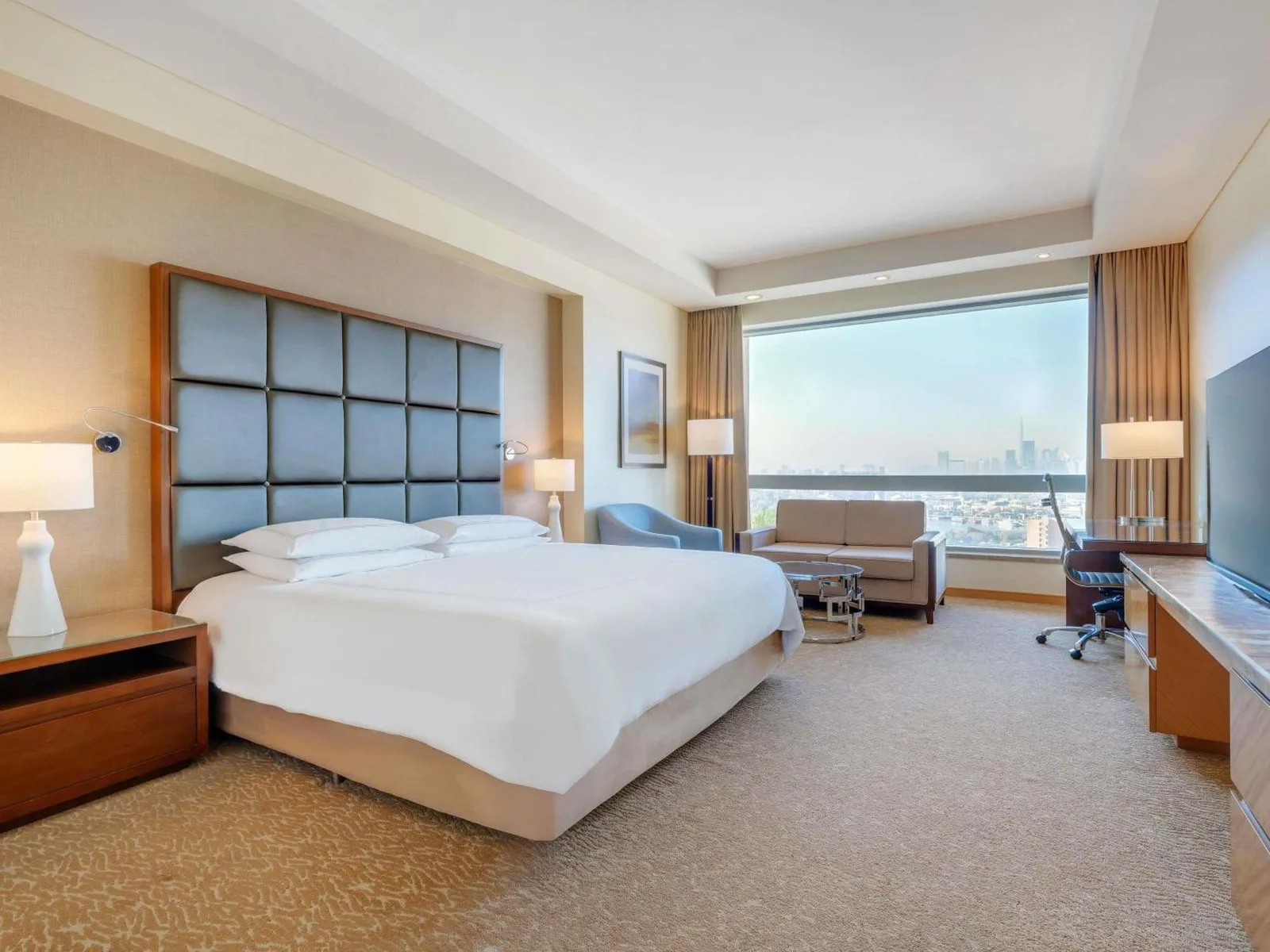 Geräumiges Gästezimmer im Swissôtel Al Ghurair Dubai mit Kingsize-Bett, Sitzbereich und Stadtblick