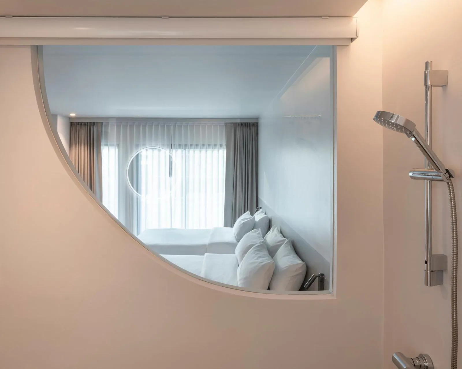 Blick ins Badezimmer durch ein gebogenes Innenfenster im Hotel Terra Nara in Pattaya, mit dem Schlafzimmer im Hintergrund.
