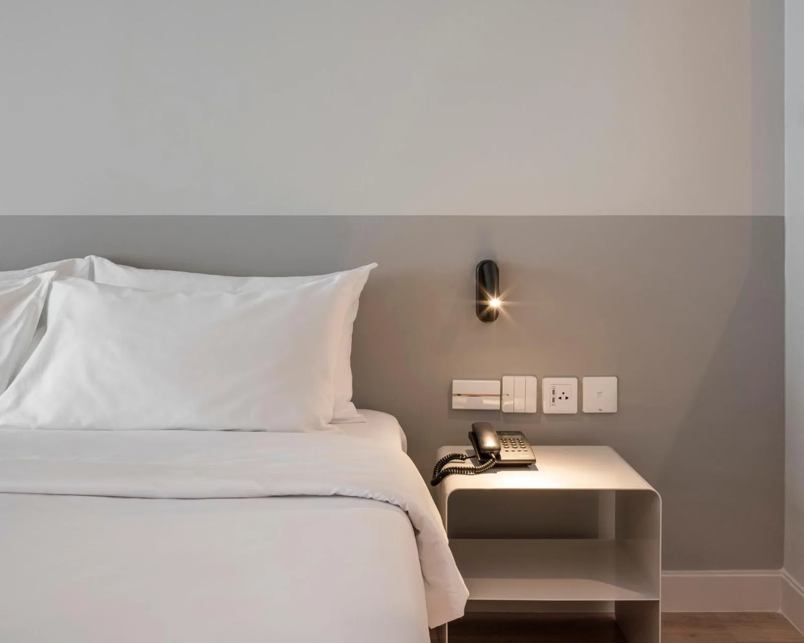 Nahaufnahme eines Betts und Nachttischs im Hotelzimmer Terra Nara Pattaya mit Lampe und Telefon.
