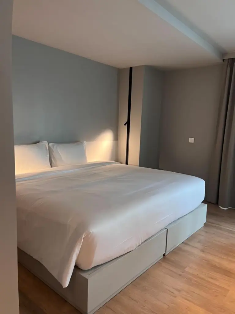 Minimalistisches Kingsize-Bett im Hotelzimmer Terra Nara Pattaya mit sanfter Beleuchtung und neutralen grauen Wänden.