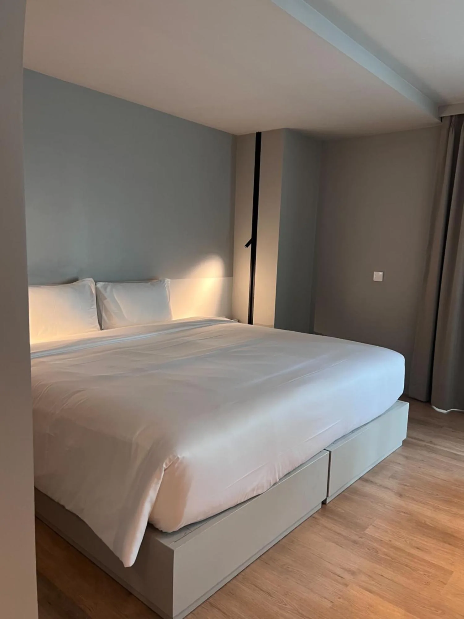 Minimalistisches Kingsize-Bett im Hotelzimmer Terra Nara Pattaya mit sanfter Beleuchtung und neutralen grauen Wänden.