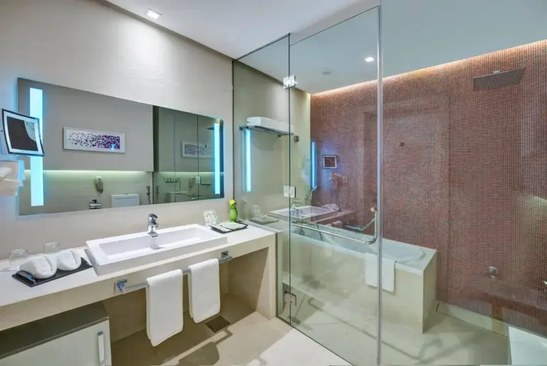 The Act Hotel Sharjah bathroom with double vanity, glass shower, and bathtub.