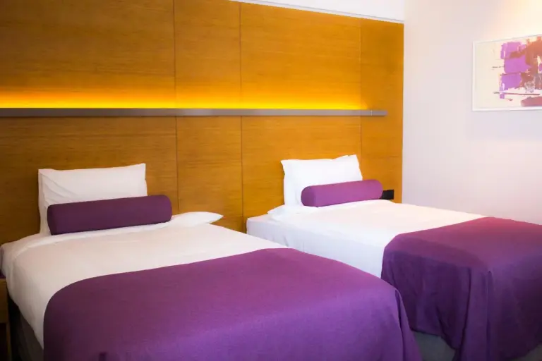 The Act Hotel Sharjah twin guest room with two beds and warm wood-accent wall.