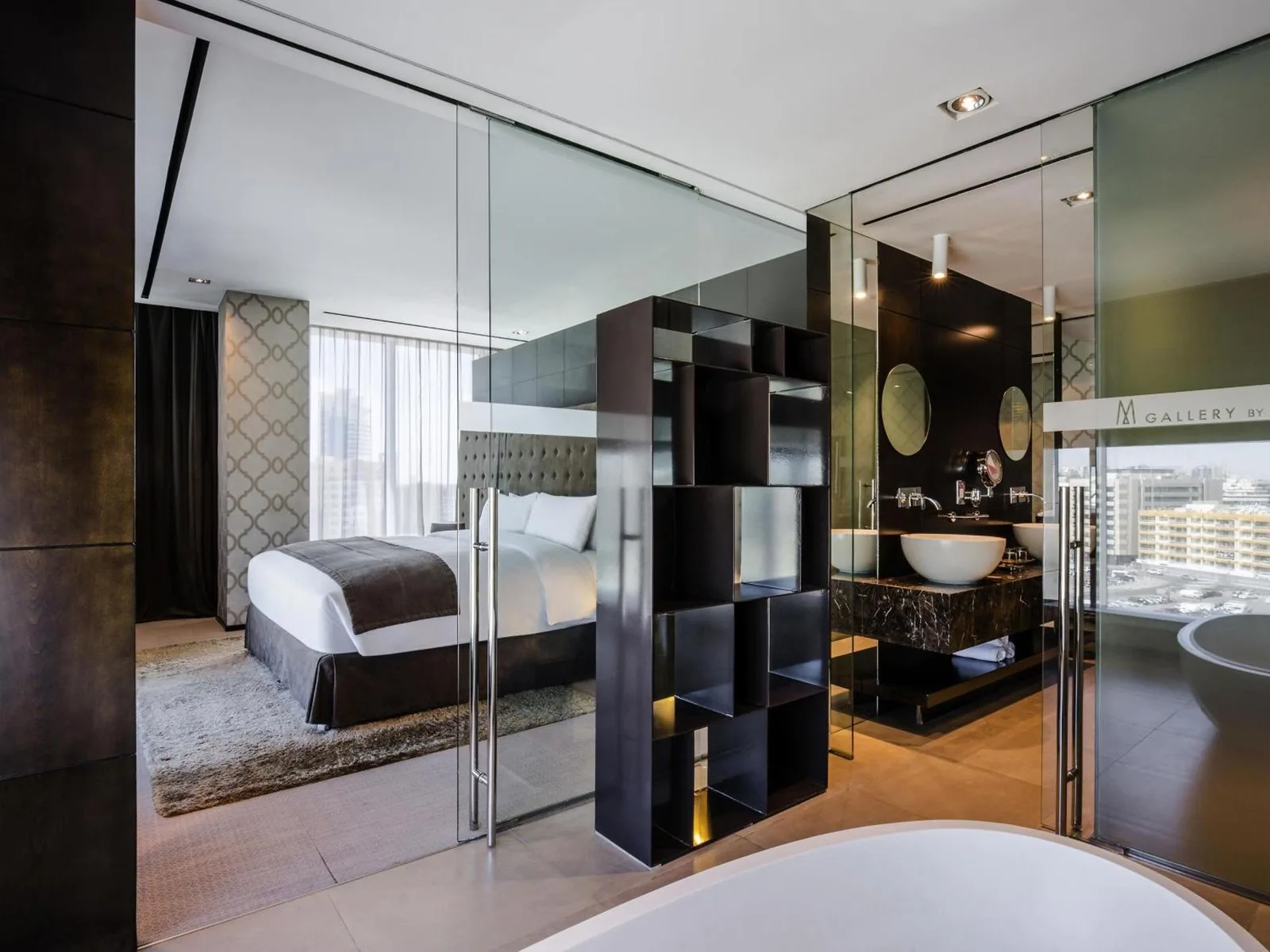 Suite bathroom and bedroom area at The Canvas Dubai - MGallery Hotel Collection in Dubai with glass walls and modern decor.