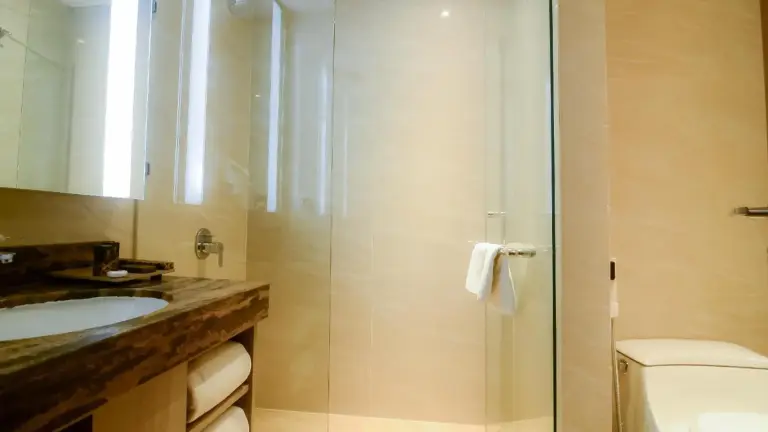 Guest bathroom at The Excelton Hotel Palembang with shower, sink, and towel rack