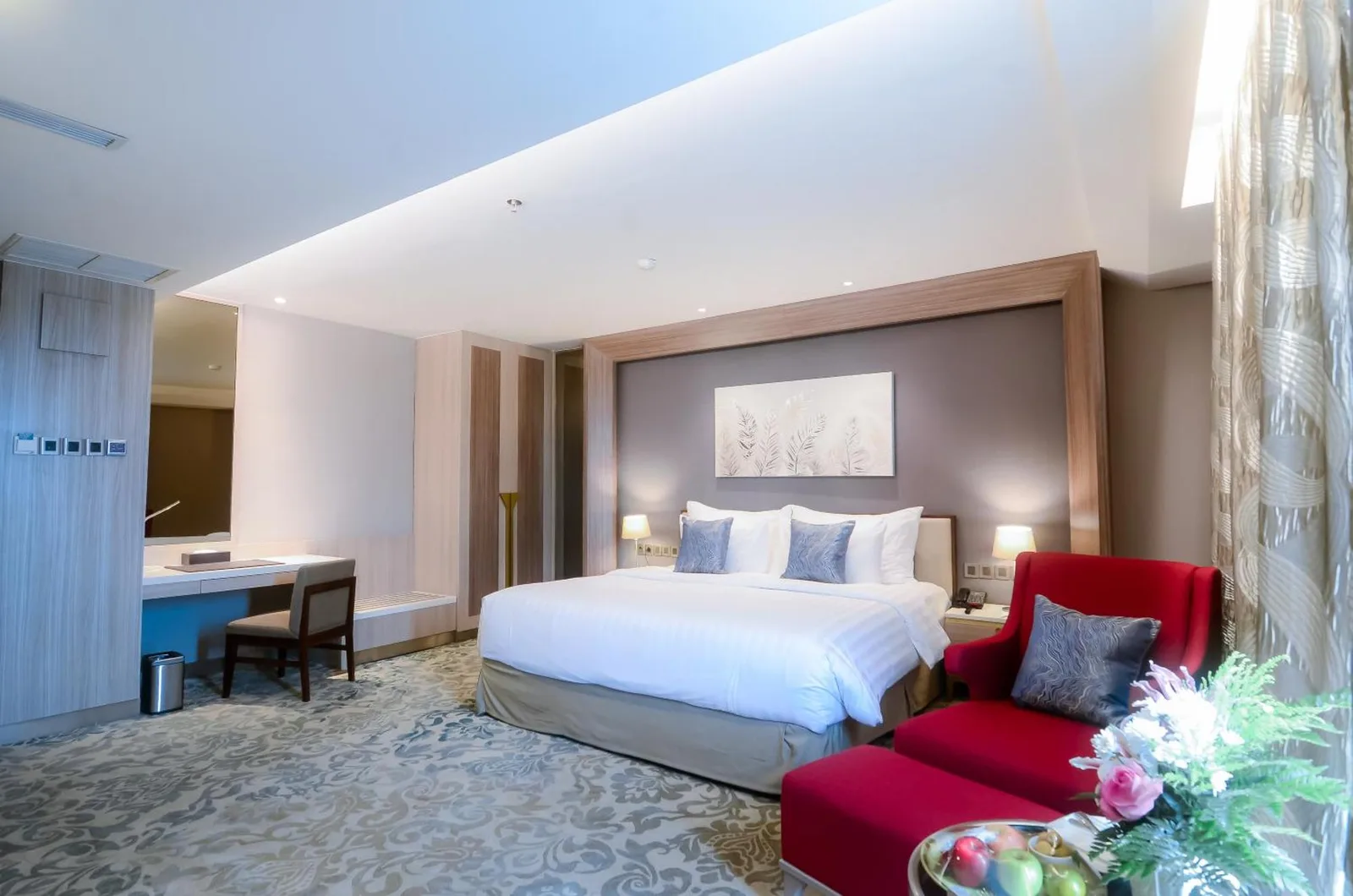 Elegant suite room at The Excelton Hotel Palembang with king bed, red armchair, and workspace