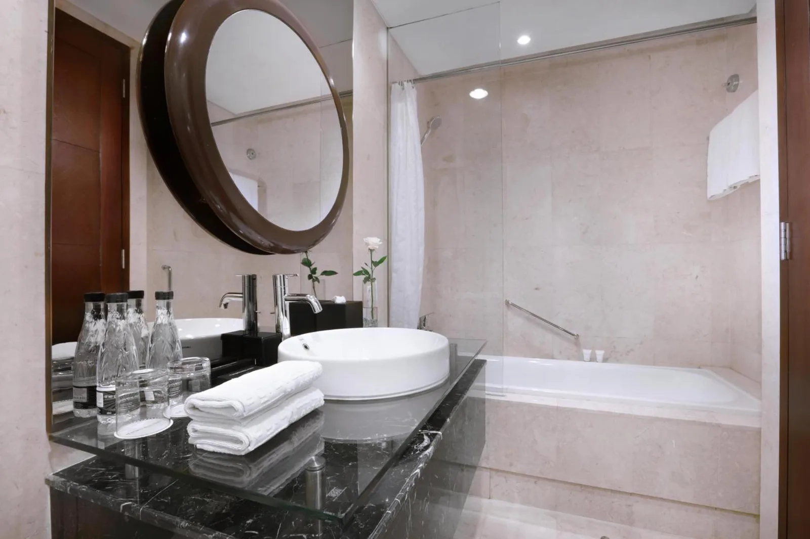 The Grove Suites by Grand Aston Jakarta bathroom vanity with round mirror, sink, and bathtub