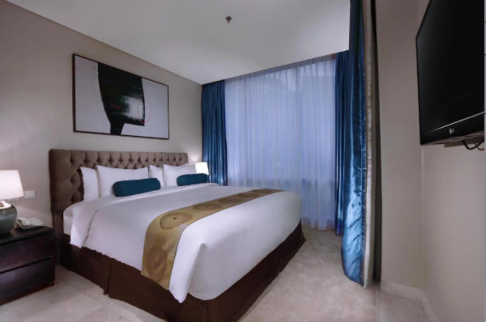 The Grove Suites by Grand Aston Jakarta bedroom with king bed, blue curtains, and wall-mounted TV