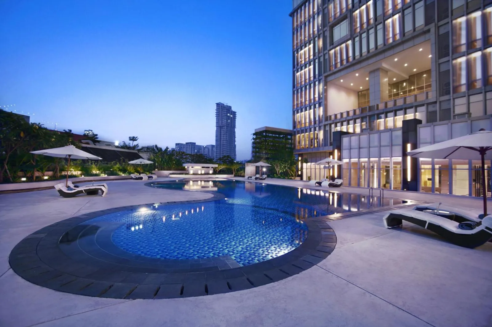 The Grove Suites by Grand Aston Jakarta outdoor swimming pool with modern hotel exterior at dusk