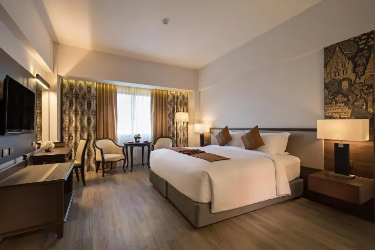 Amplia habitación de huéspedes en The Heritage Chiang Rai Hotel and Convention con una cama king, zona de estar y decoración moderna y cálida.