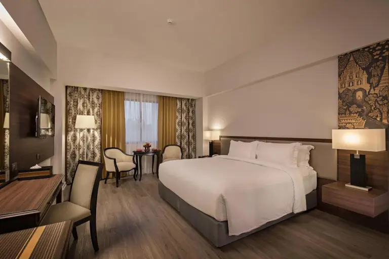 Habitación king en The Heritage Chiang Rai Hotel and Convention con una cama grande, escritorio y zona de estar.