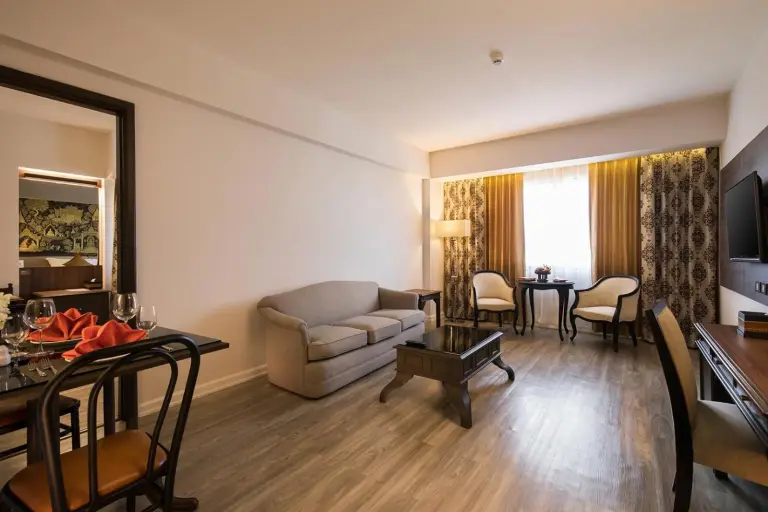 Sala de estar de la suite en The Heritage Chiang Rai Hotel and Convention con sofá, mesa de centro, zona de comedor y TV.