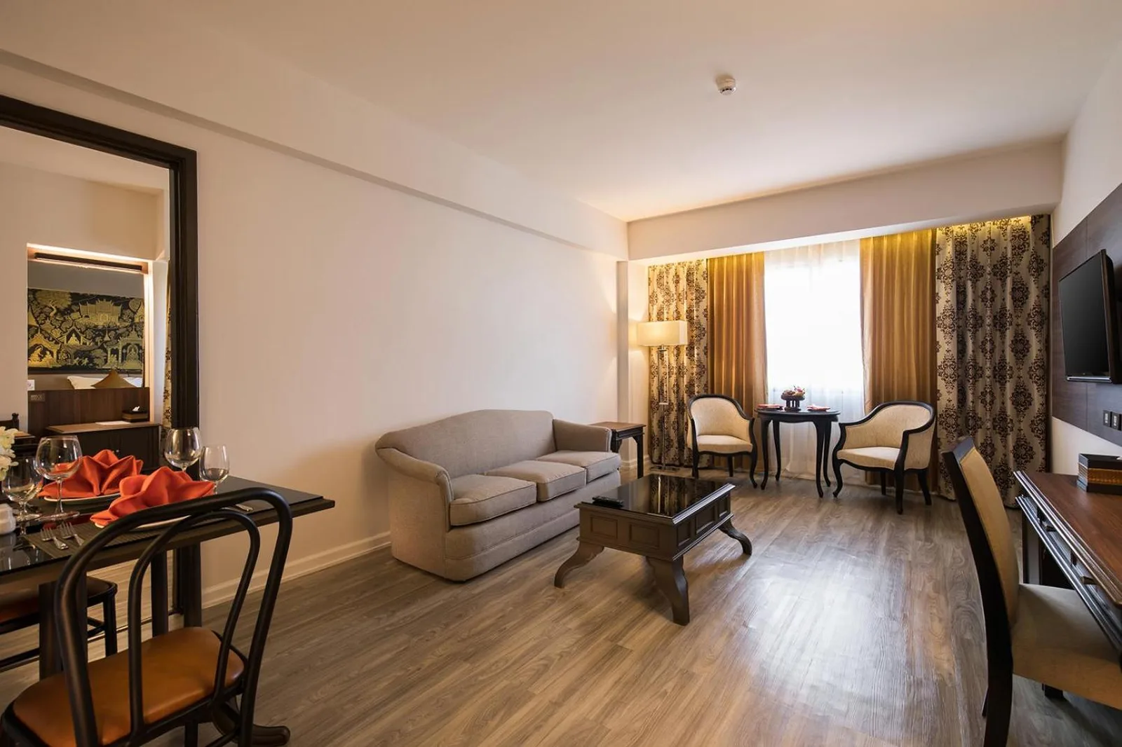 Sala de estar de la suite en The Heritage Chiang Rai Hotel and Convention con sofá, mesa de centro, zona de comedor y TV.