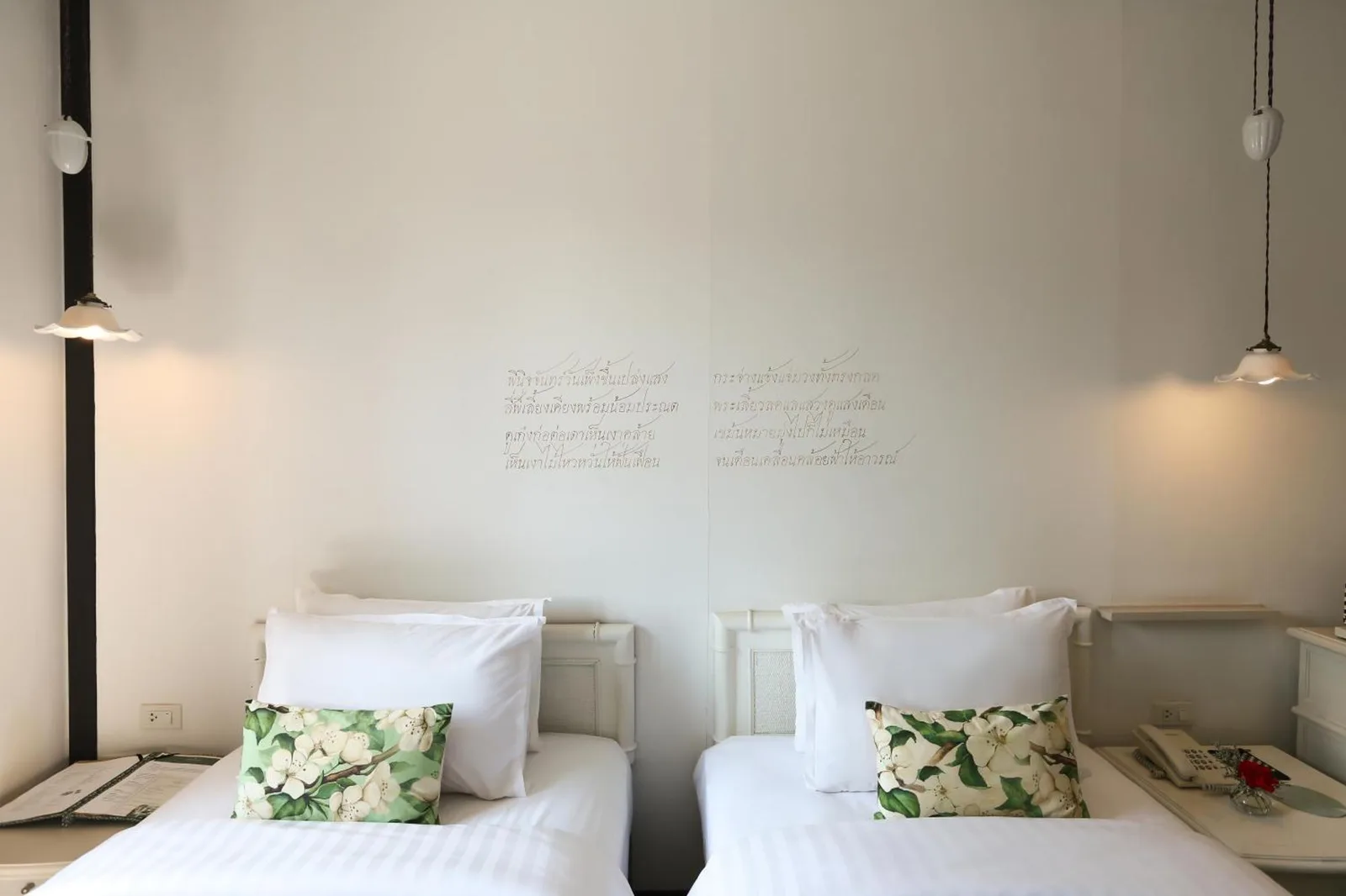 Twin beds with floral pillows in a minimalist room at The Raweekanlaya Bangkok Wellness Cuisine Resort Bangkok