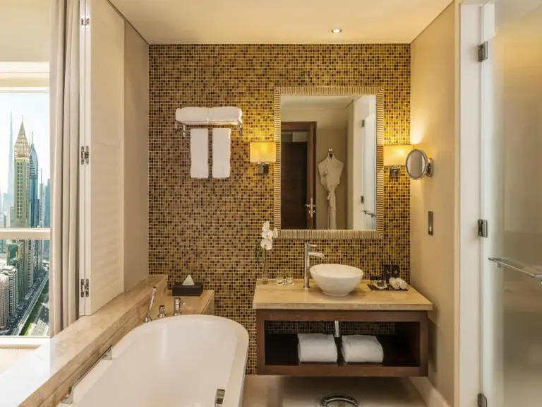 Mosaic-tiled bathroom at The Tower Plaza Hotel Dubai with a bathtub, sink vanity, and mirror.