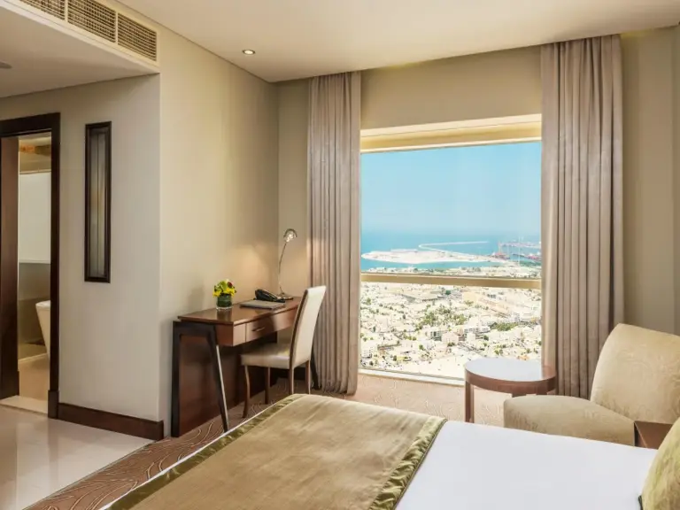 Guest room at The Tower Plaza Hotel Dubai with a desk, seating area, and panoramic sea and city view.