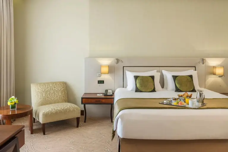 Elegant bedroom at The Tower Plaza Hotel Dubai with a king bed, bedside lighting, and breakfast tray.