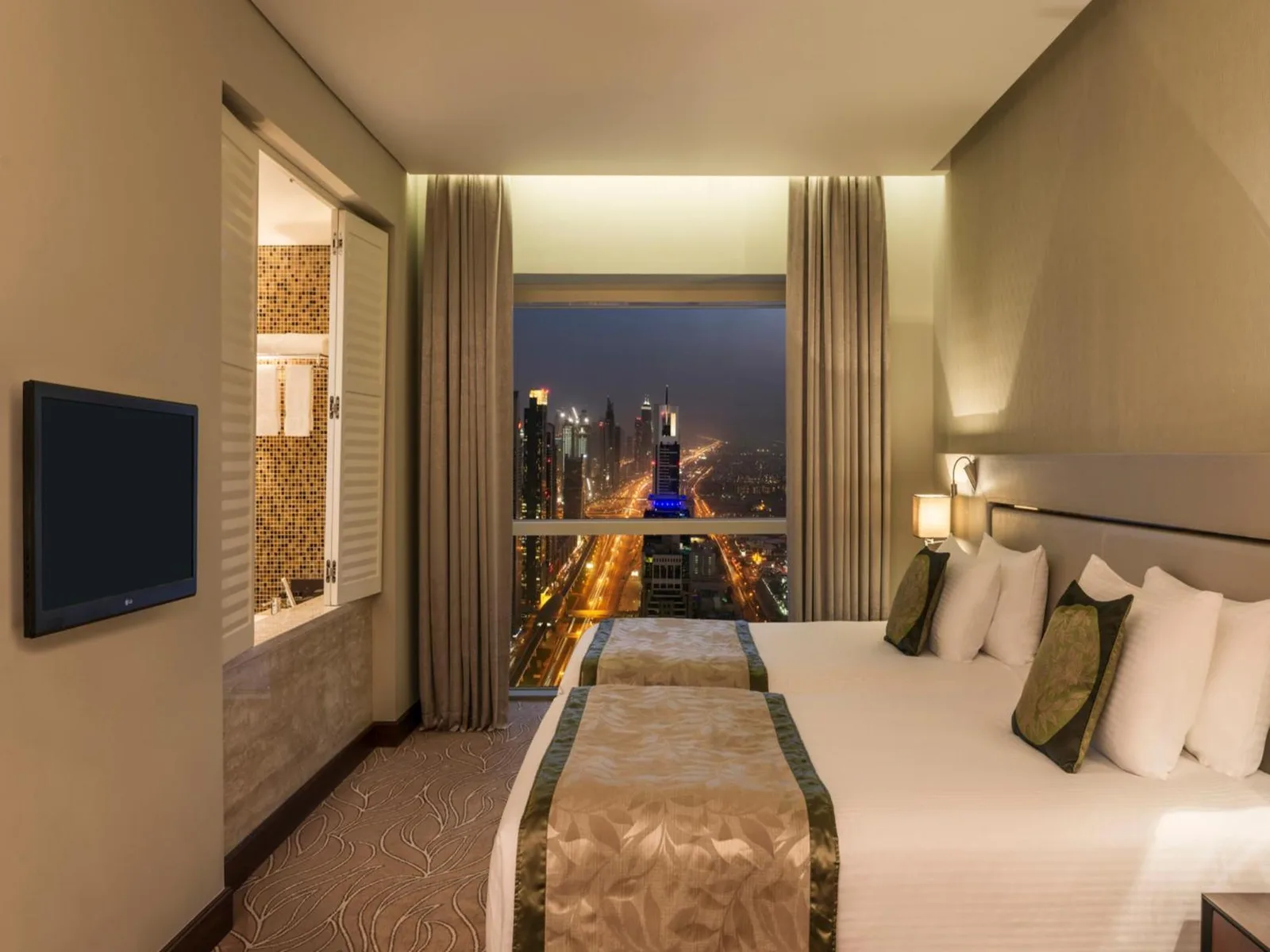 Modern bedroom at The Tower Plaza Hotel Dubai with a city skyline night view through large windows.
