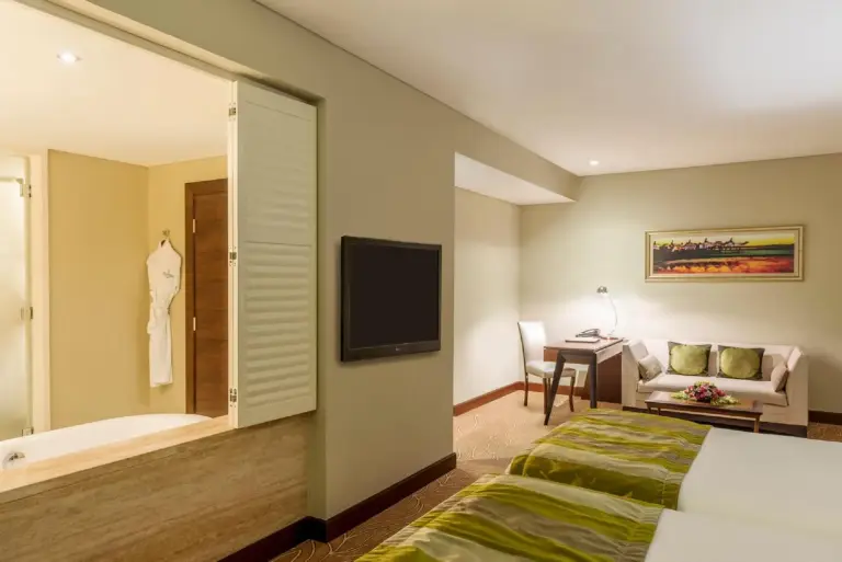 Studio-style suite at The Tower Plaza Hotel Dubai with a bed, sofa, desk, and wall-mounted TV.