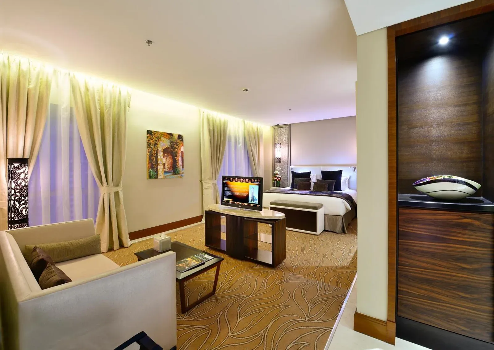 Spacious suite lounge at The Tower Plaza Hotel Dubai with sofa seating, a dining desk, and a bed area.