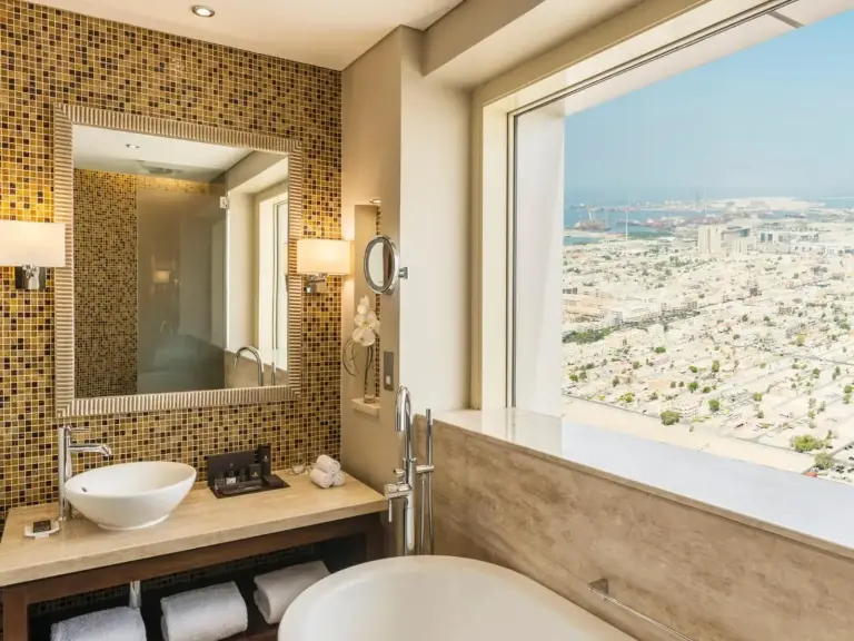 Spacious bathroom at The Tower Plaza Hotel Dubai with a bathtub and large window overlooking Dubai.