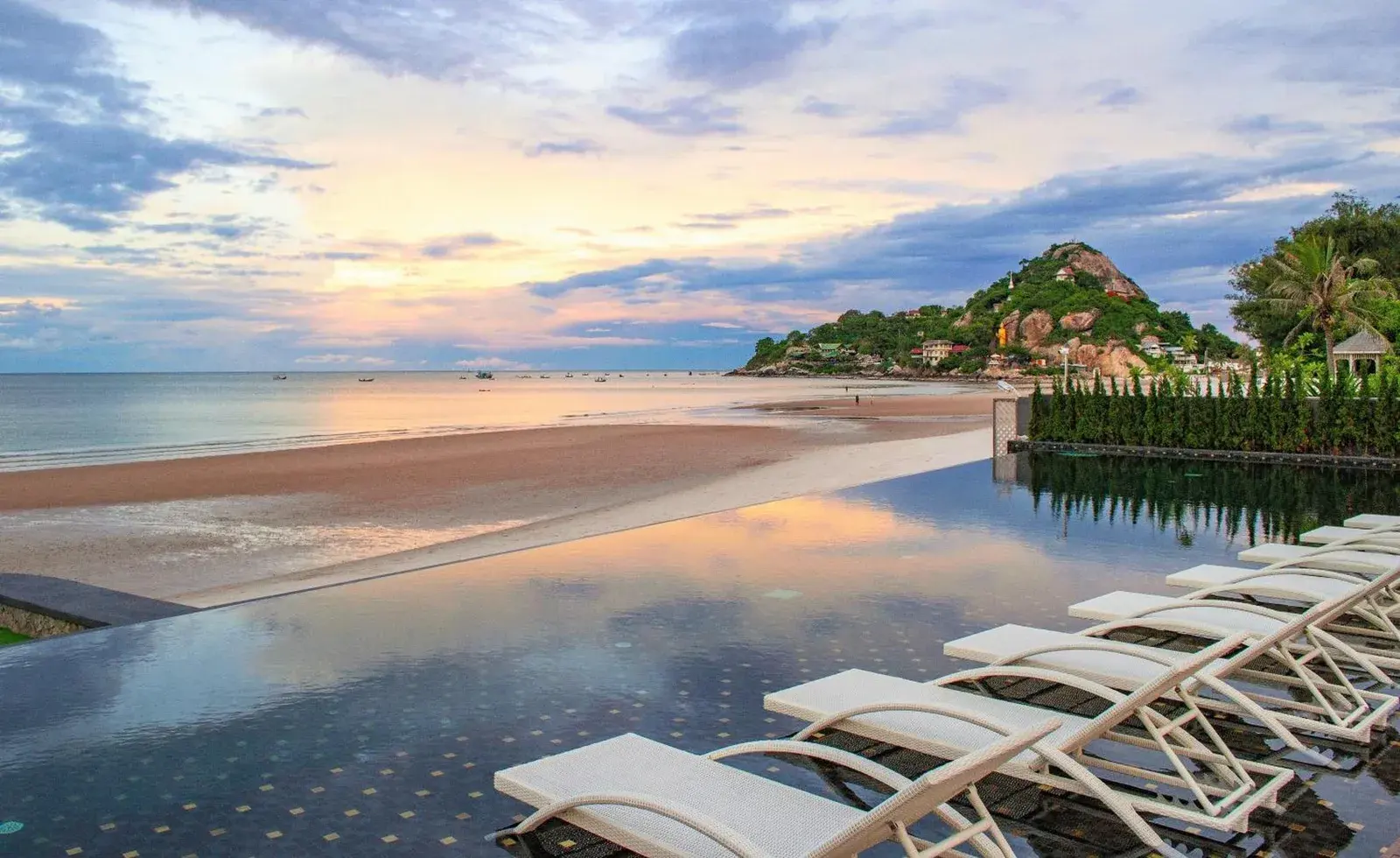 Impresionante vista de la piscina infinita en The Yana Villas Hua Hin con atardecer en la playa
