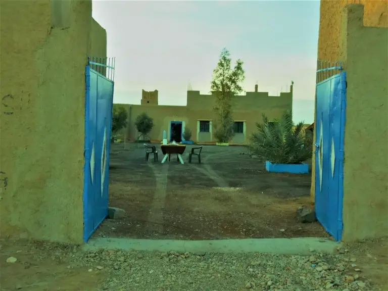 Puertas azules abiertas que conducen al patio de Tifinagh Guest House en Merzouga