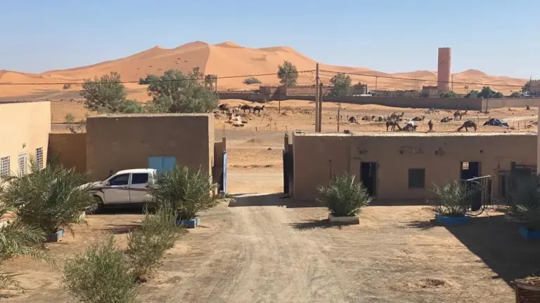 Vista exterior de Tifinagh Guest House en Merzouga con patio, entorno desértico y dunas de arena al fondo