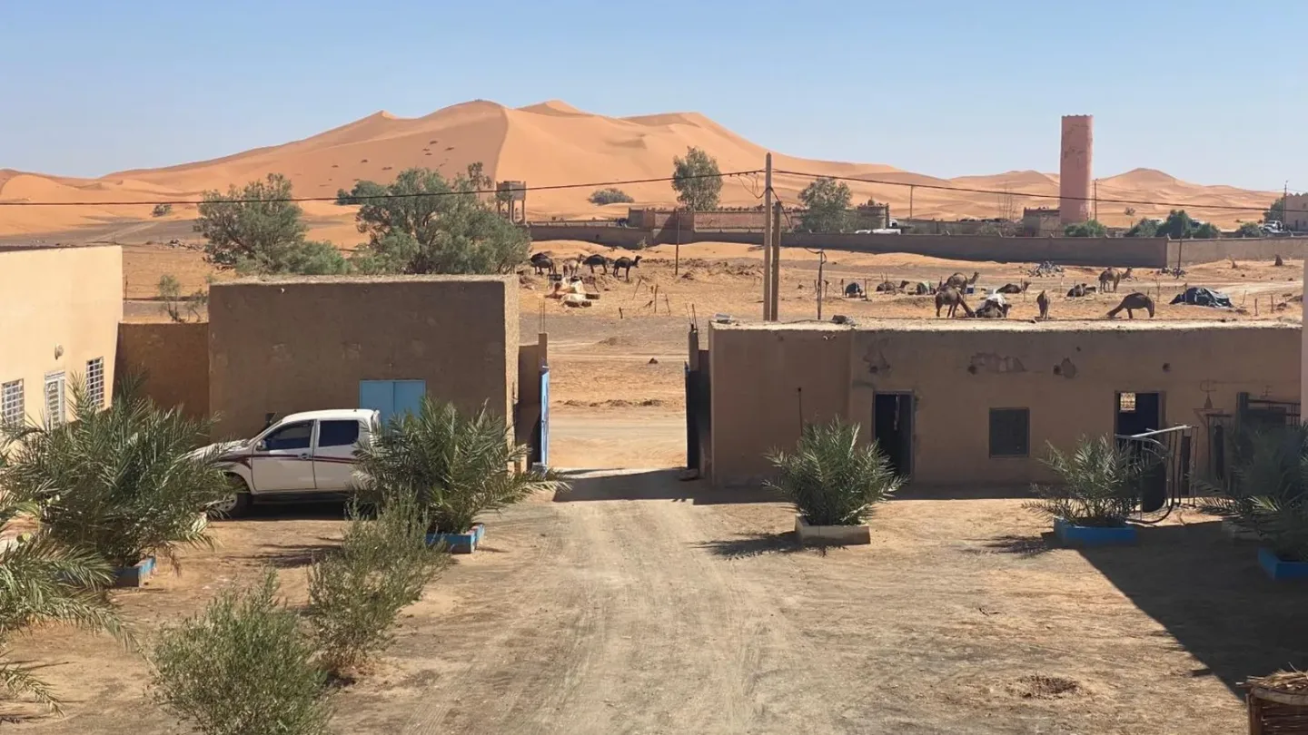 Vista exterior de Tifinagh Guest House en Merzouga con patio, entorno desértico y dunas de arena al fondo
