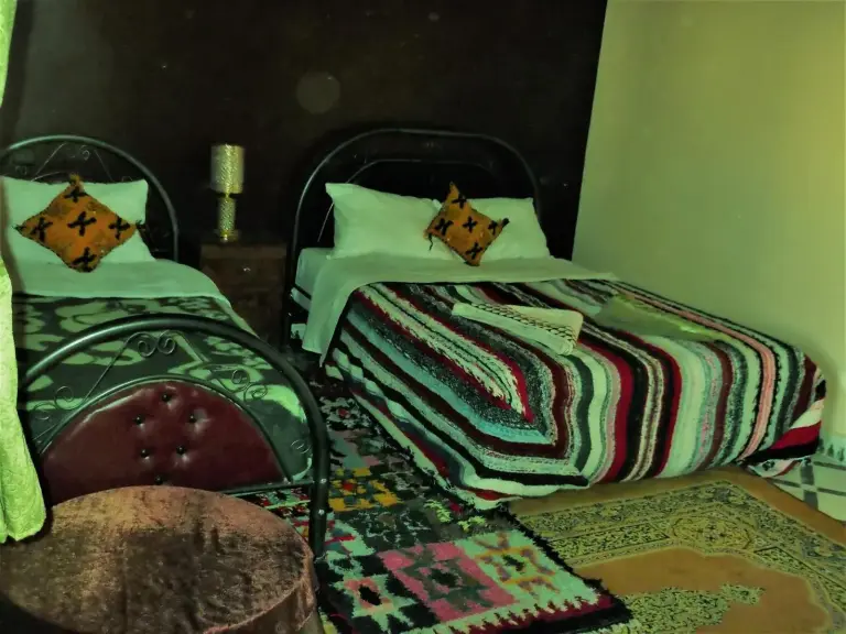 Dormitorio twin en Tifinagh Guest House en Merzouga con ropa de cama a rayas y textiles marroquíes tradicionales