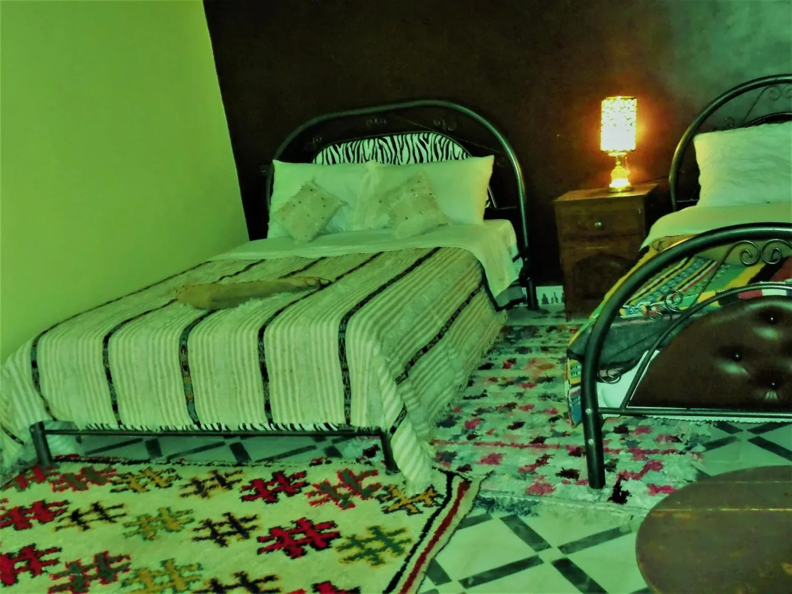 Habitación twin en Tifinagh Guest House en Merzouga con dos camas individuales, lámpara de noche y alfombras estampadas
