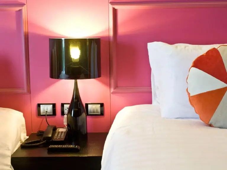 Nahaufnahme eines Betts mit rosa Wanddekoration und Nachttischlampe im Tsix5 Phenomenal Hotel Pattaya in Pattaya.