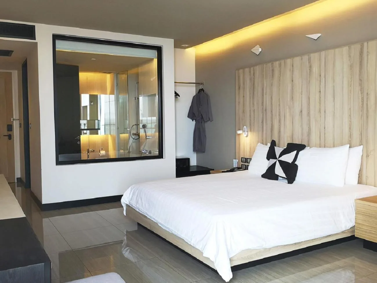 Zimmer mit Kingsize-Bett im Tsix5 Phenomenal Hotel Pattaya in Pattaya mit minimalistischer moderner Einrichtung und Fenster im Badezimmer.