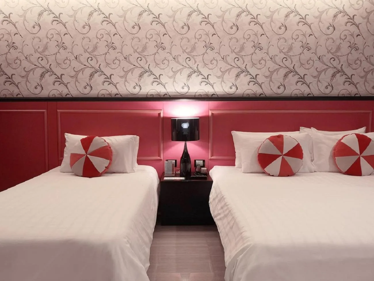 Zwei Betten mit gemusterter Tapete im Tsix5 Phenomenal Hotel Pattaya in Pattaya und Nachttischlampe dazwischen.