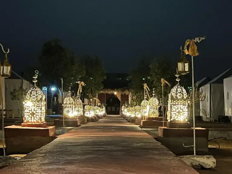 Tudert Luxury Camp – Merzouga, Morocco hotel – a resort entrance with a resort with chairs and umbrellas at Tudert Luxury Camp in Merzouga