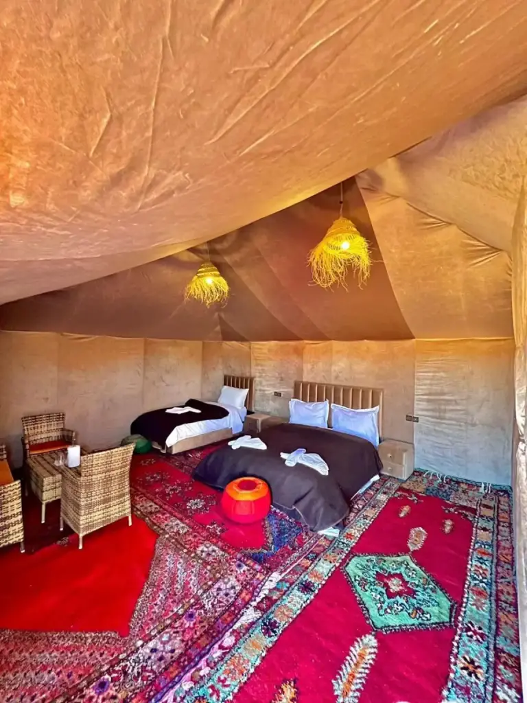 Triple bed tent suite at Tudert Luxury Camp in Merzouga with patterned carpets and warm lighting