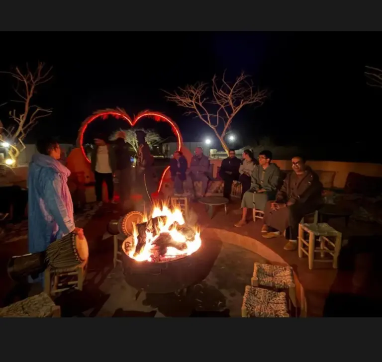 Salón con hoguera en Ultimate Luxury Camp en Merzouga con huéspedes sentados alrededor de un fuego por la noche