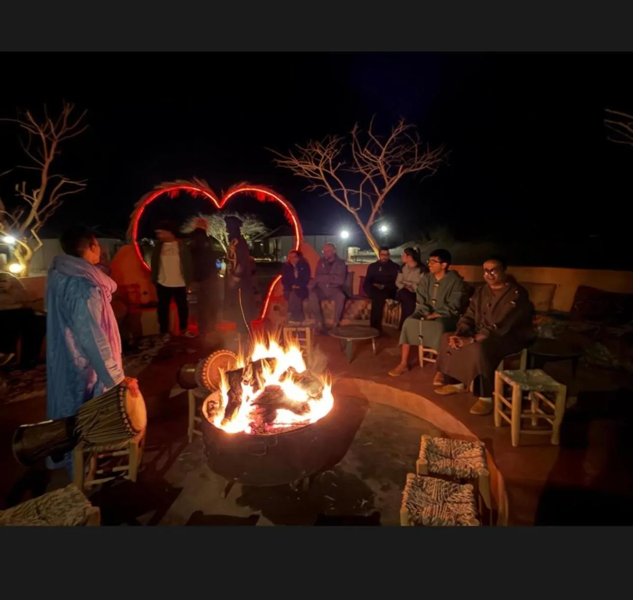 Salón con hoguera en Ultimate Luxury Camp en Merzouga con huéspedes sentados alrededor de un fuego por la noche