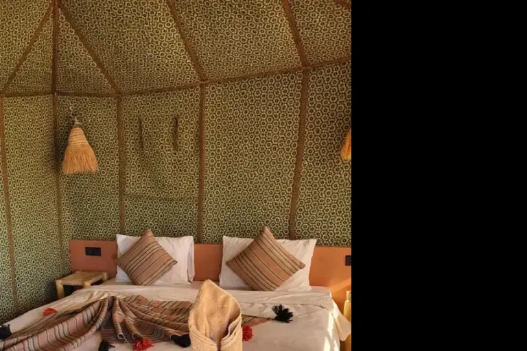 Acogedor dormitorio de tienda en Ultimate Luxury Camp en Merzouga con una cama perfectamente hecha y detalles tradicionales marroquíes