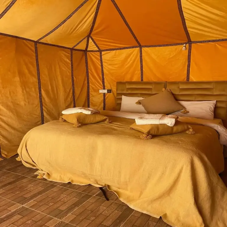 Stilvolles Zelt-Schlafzimmer im Unique Sahara Camp in Merzouga mit warm getönter Bettwäsche und Design einer Wüstenlodge