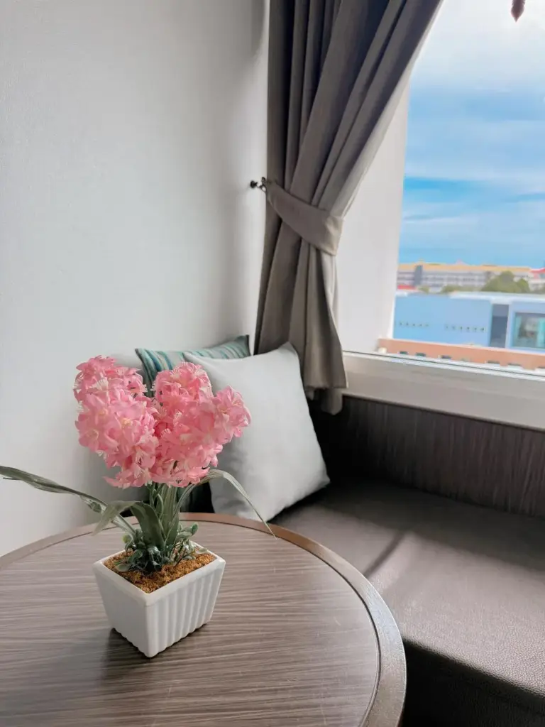Gemütliche Sitzecke im Vareena Palace Hotel in Pattaya mit Beistelltisch, Blumen und Blick aus dem Fenster.
