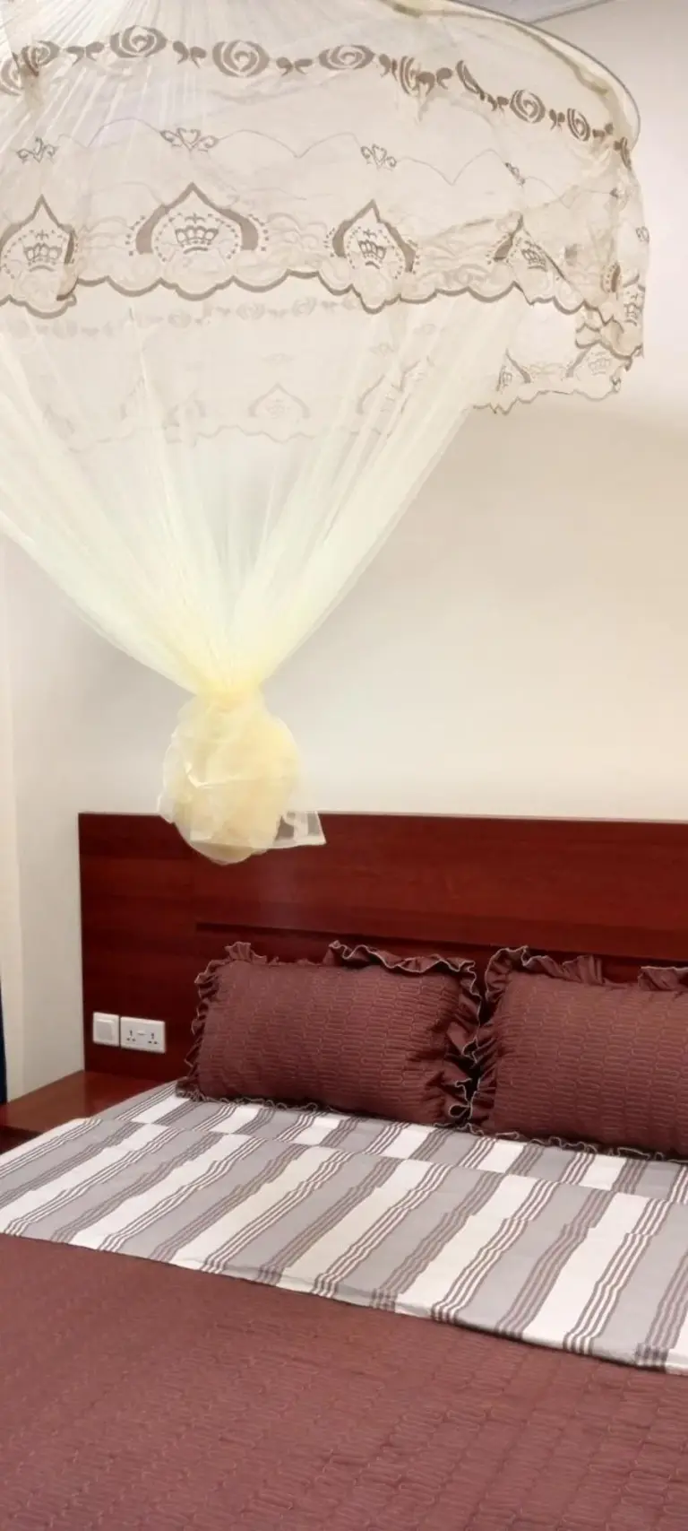 Nahaufnahme des Schlafzimmers im VENUS APARTMENT Kigali in Nyamata mit Bett, Kopfteil und Moskitonetz.
