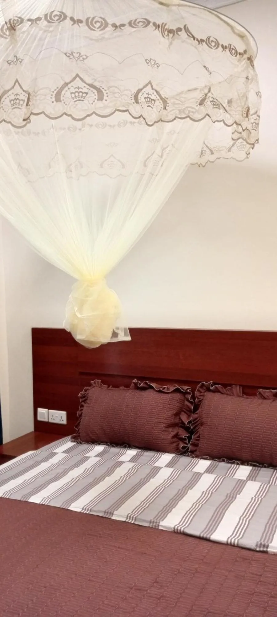 Nahaufnahme des Schlafzimmers im VENUS APARTMENT Kigali in Nyamata mit Bett, Kopfteil und Moskitonetz.
